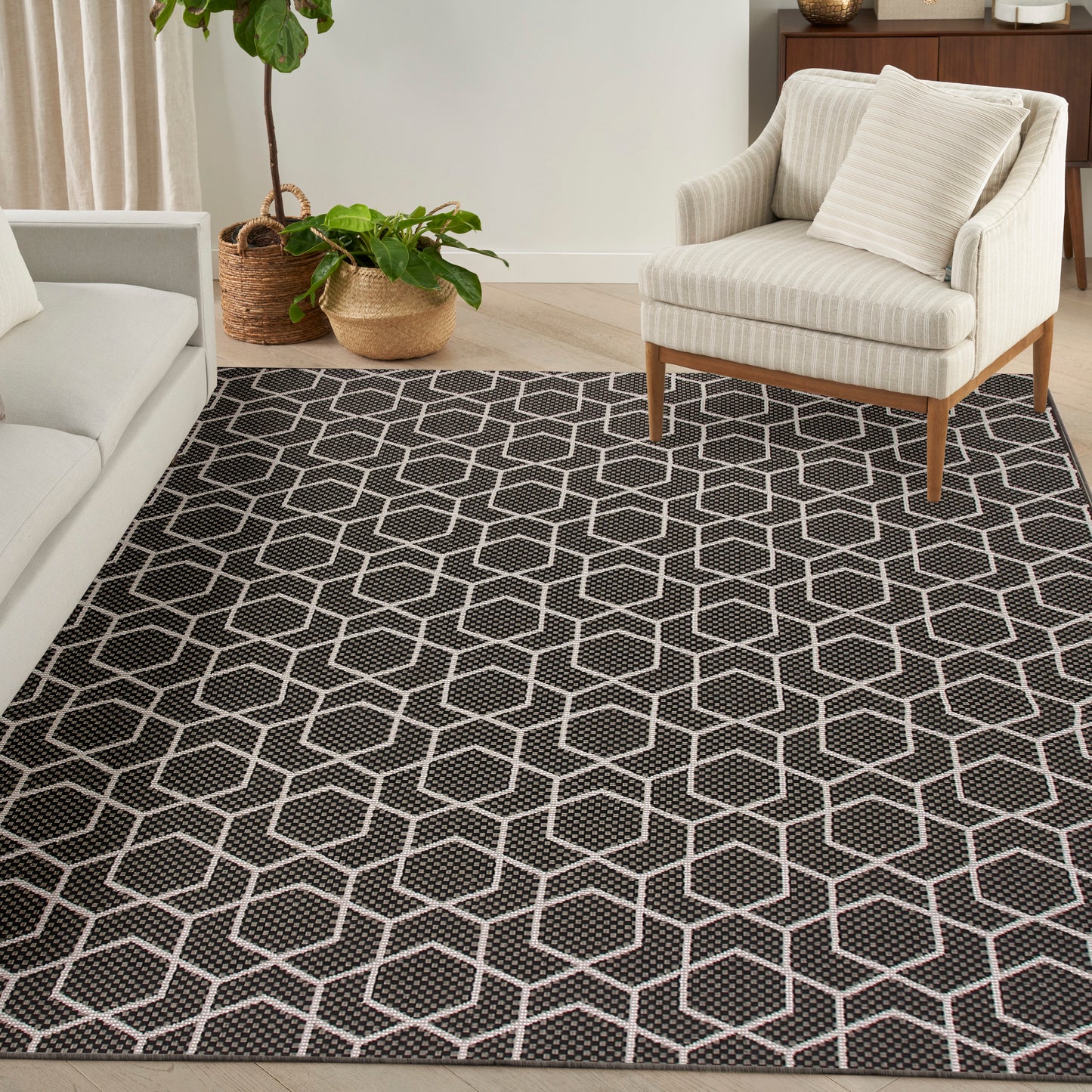 Charcoal rug with white geometric hexagon pattern in a modern living room, paired with beige armchair and potted plants.