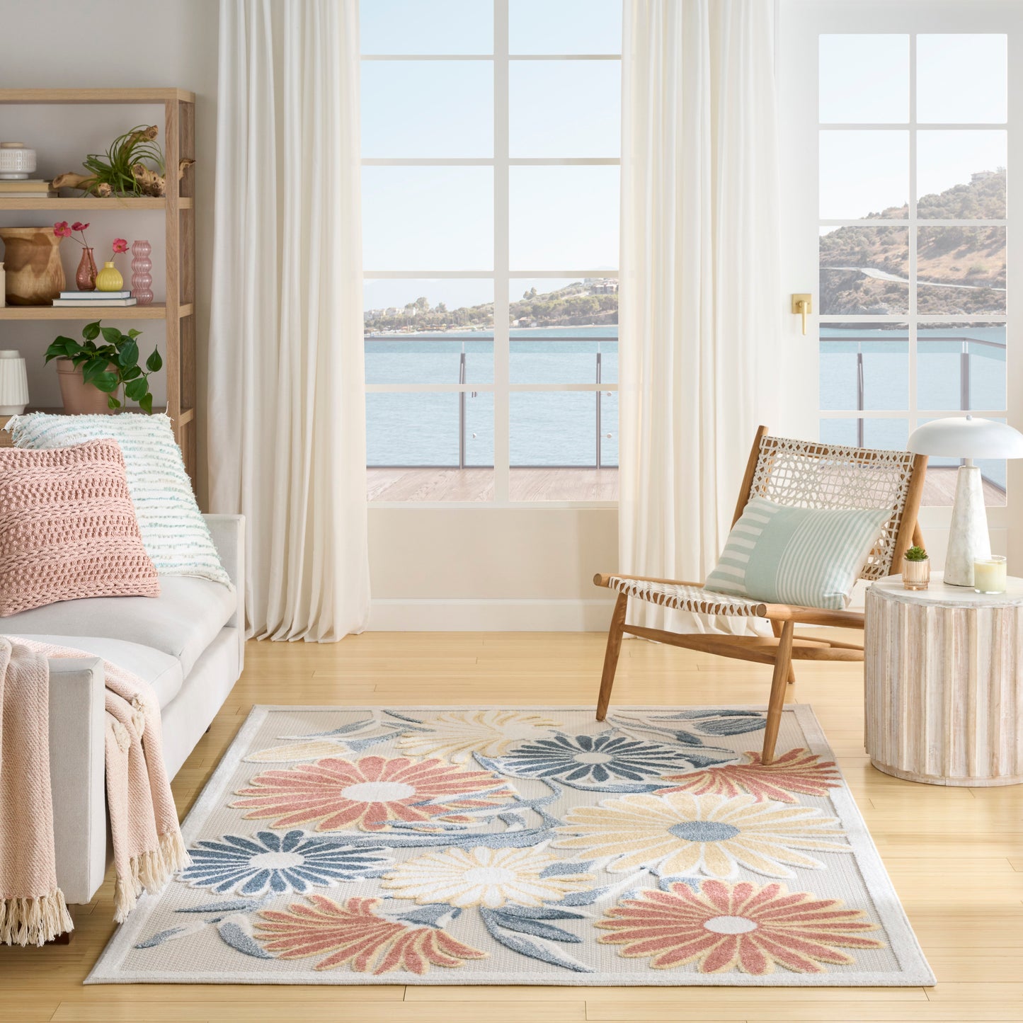 Soft pastel floral area rug in a bright coastal living room with a wicker chair, cream curtains and ocean view.