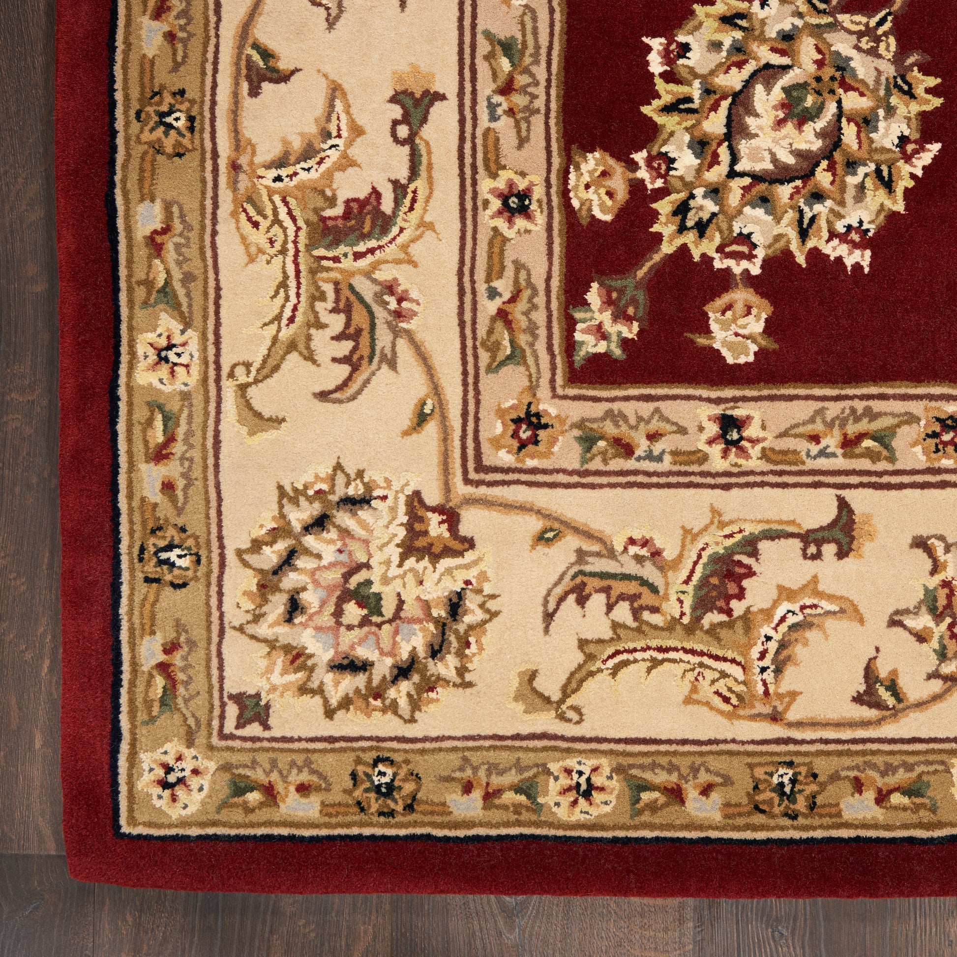 Traditional Persian-style area rug with cream/beige border, ivory floral vines, and a red inner field on dark wood floor.