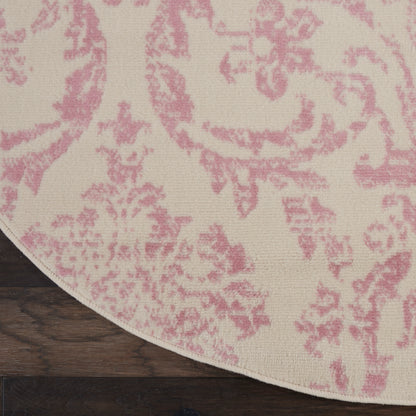 Round area rug with pink damask pattern on cream background, placed on dark wood floor.