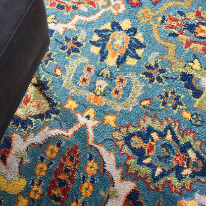 Vibrant Persian-style area rug with blue base and bright floral motifs in yellow, orange, red; dark furniture leg visible.