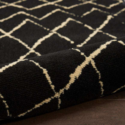 Black area rug with cream diamond lattice pattern; plush woven texture, rolled corner on wooden floor.