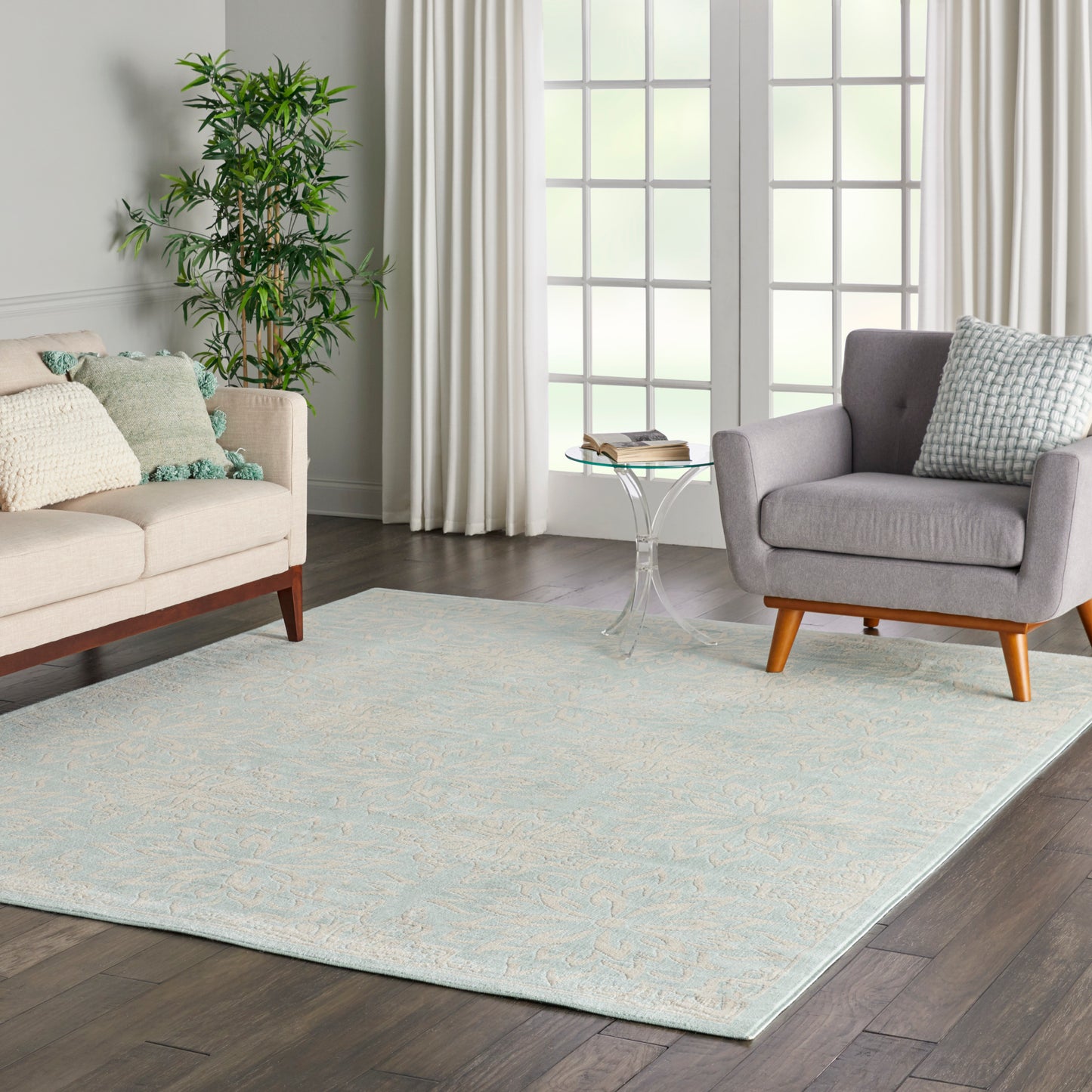 Light blue patterned area rug in a modern living room with a beige sofa, gray armchair, glass side table, and a plant.