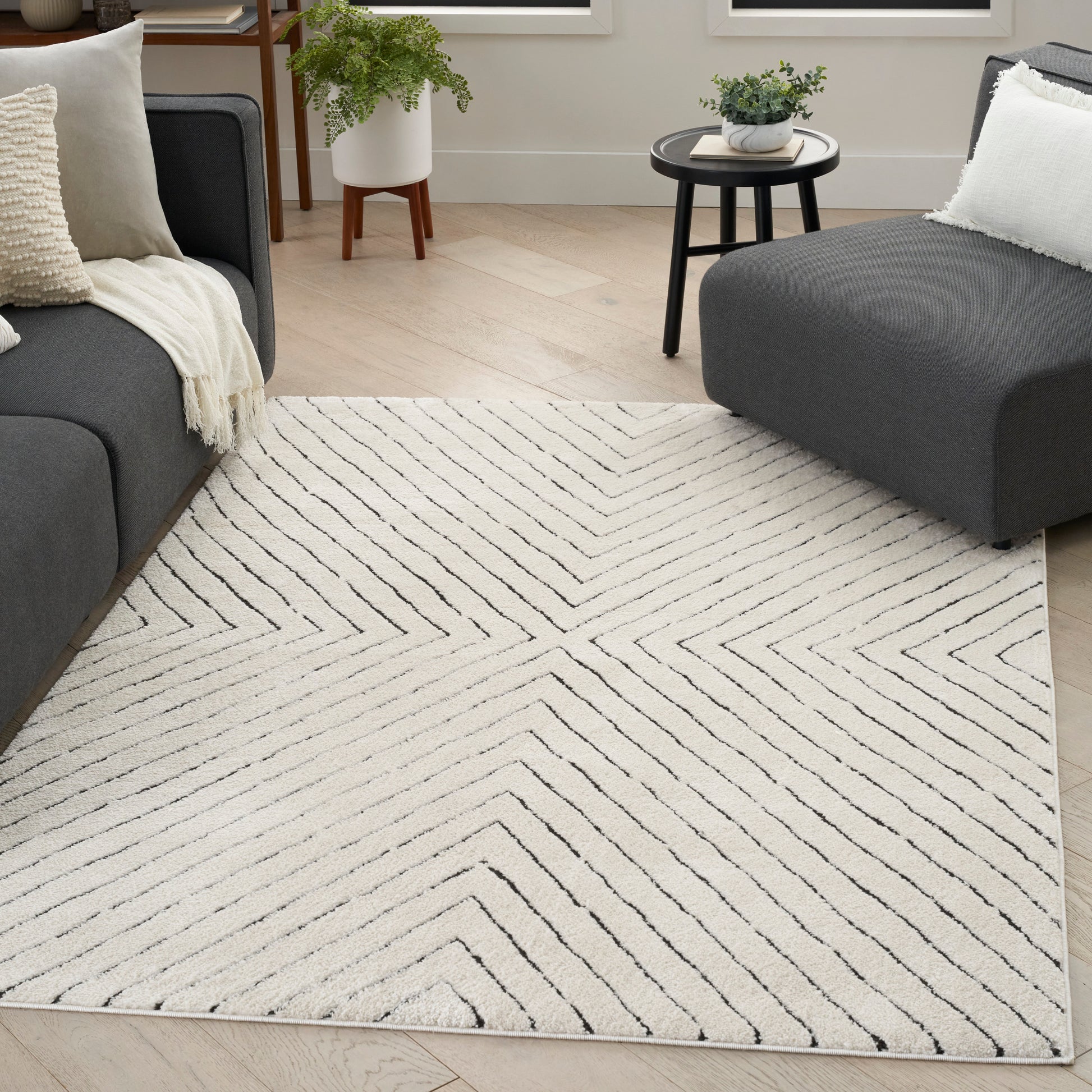 Cream rug with black chevron lines in a modern living room with dark gray sofas and a round coffee table.