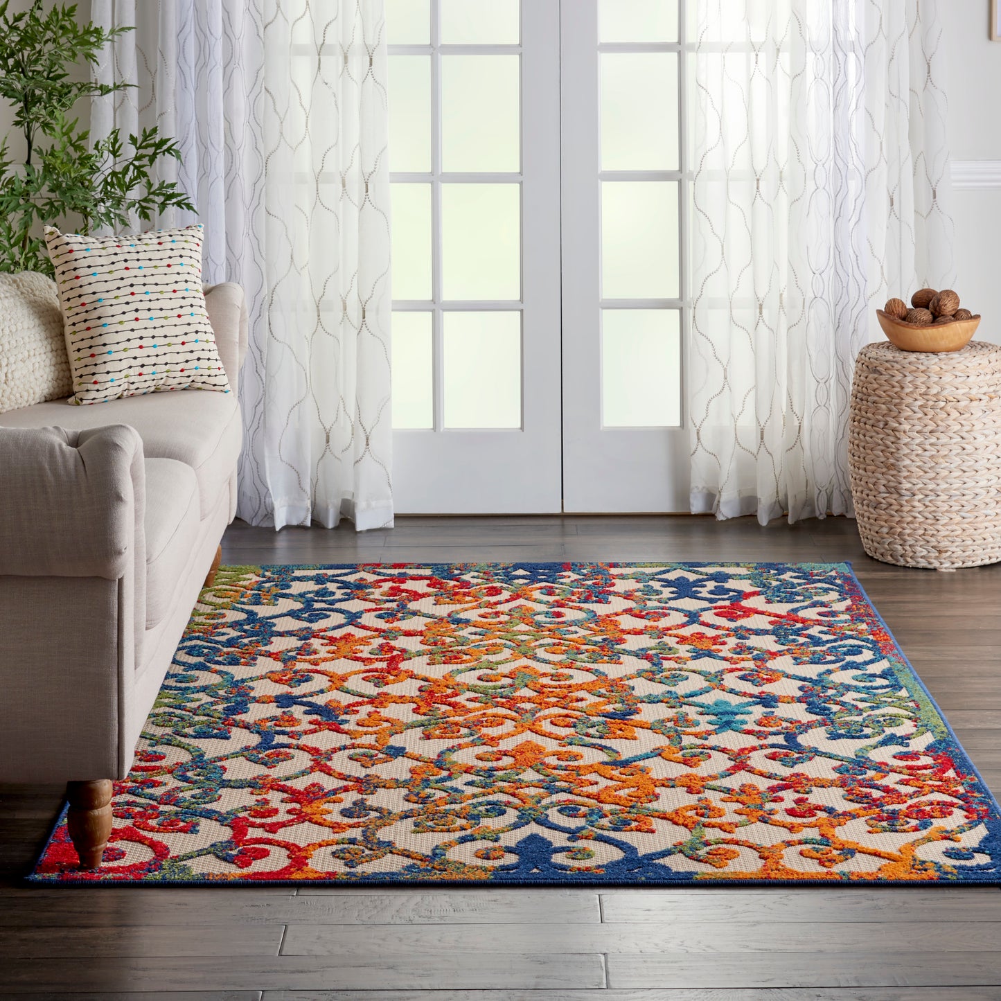 Vibrant multicolor woven area rug with interlaced floral pattern in red, blue, orange and yellow on a dark wood floor.