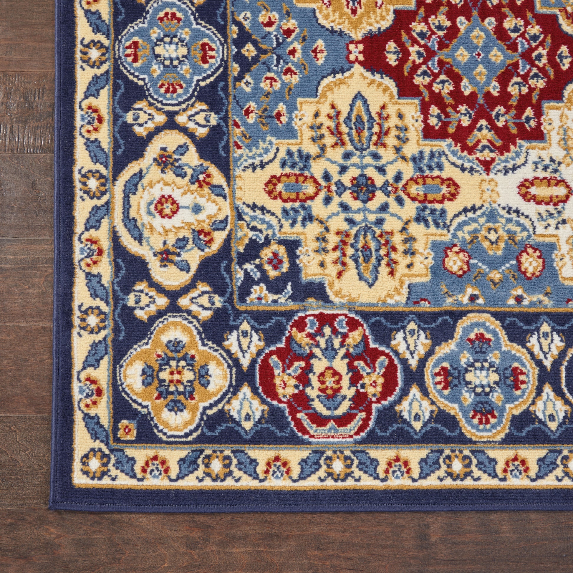Corner view of ornate oriental rug with blue, ivory, red floral medallion border on dark wood floor.