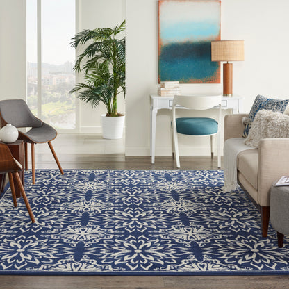 Bright living room with a blue and white patterned rug, mid-century chairs, white desk, blue chair, plant, abstract art.