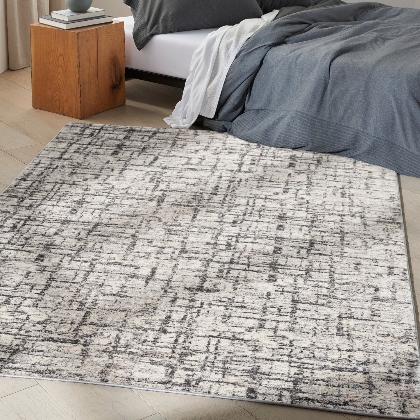 Rectangular gray and cream abstract-pattern area rug on light wood floor in a modern bedroom.