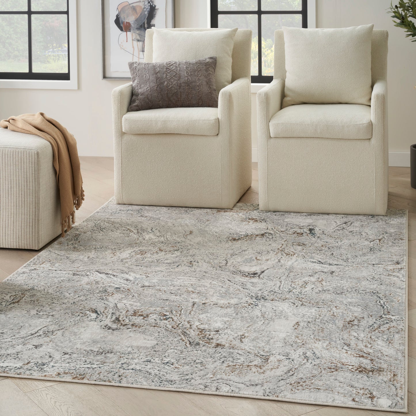 Two cream boucle armchairs with beige cushions, a beige throw on the ottoman, and a gray marble-pattern rug.