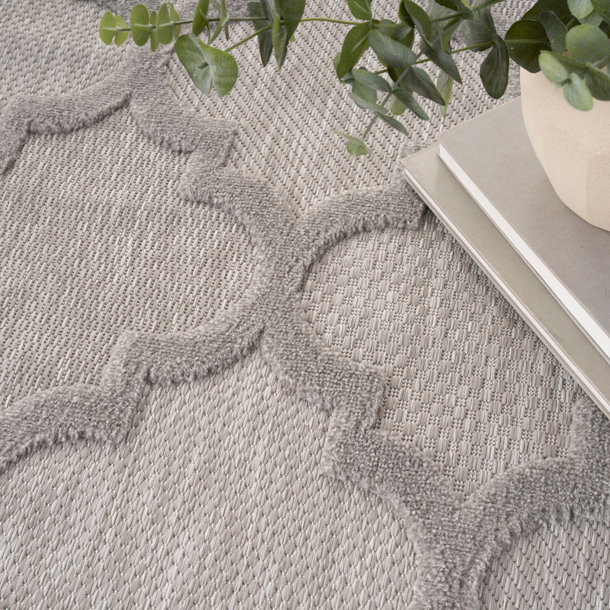 Gray woven area rug with raised quatrefoil pattern; modern textured decor, shown with plant and books.