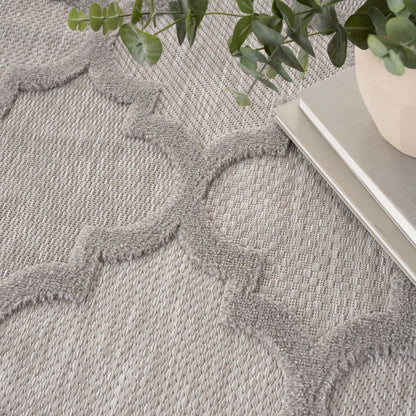 Gray woven area rug with raised quatrefoil pattern; modern textured decor, shown with plant and books.