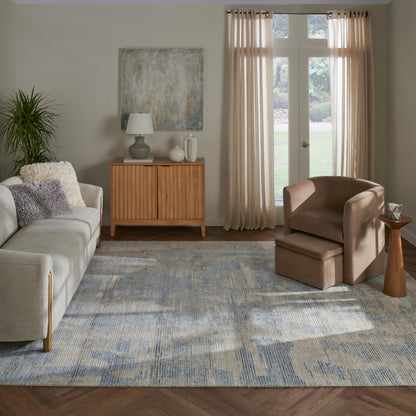 Cozy living room with light gray sofa, beige armchair & ottoman, wooden sideboard, abstract art, plant, blue-gray rug.