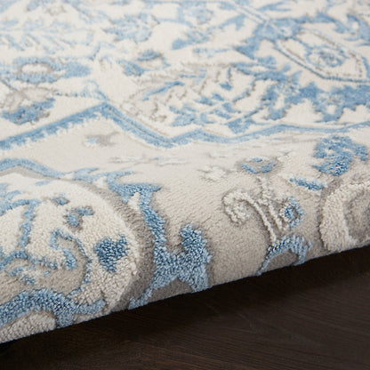 Blue and ivory ornate area rug with floral motif, soft tufted pile, rolled edge on dark wood floor.