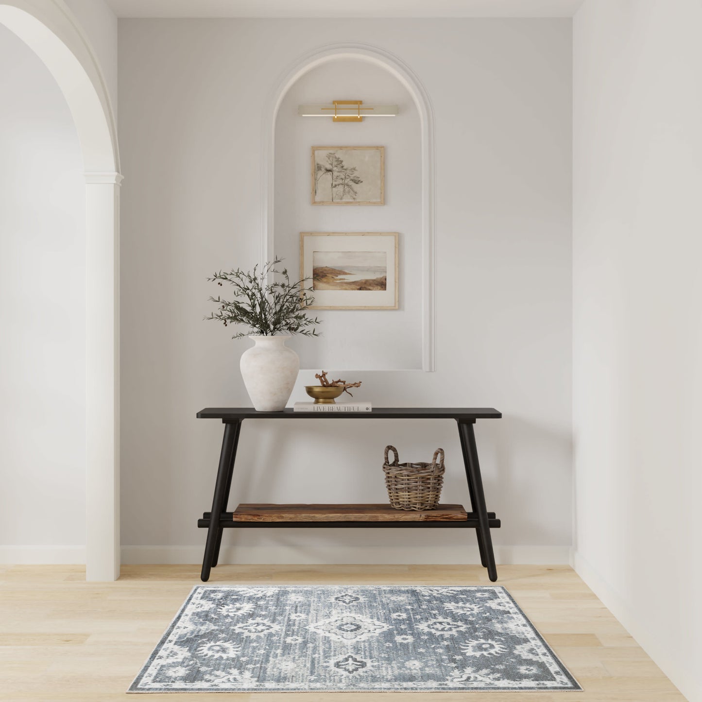Dark wood console with lower shelf, white vase with branches, woven basket, arched wall niche with framed art, blue patterned rug.