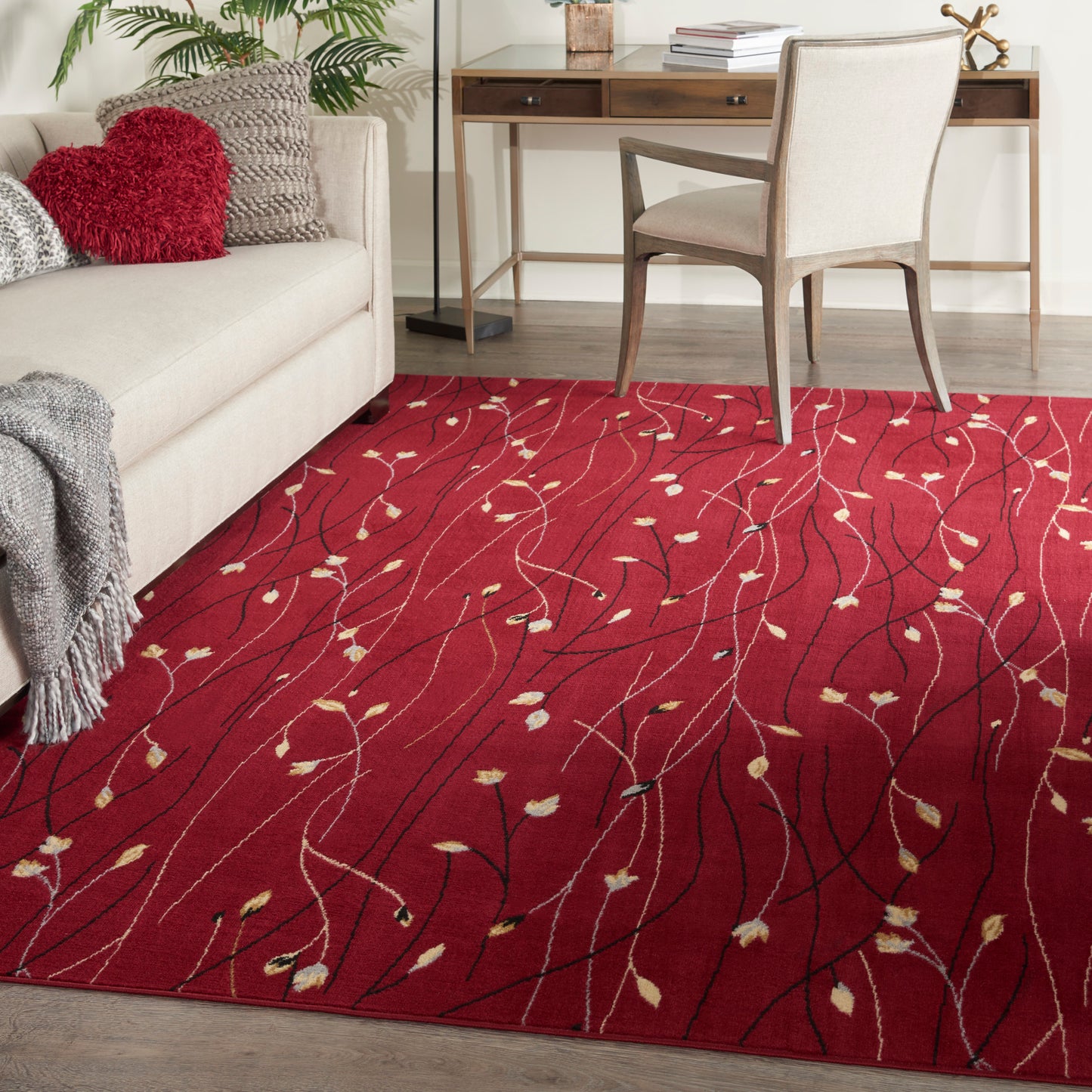Red area rug with cream leaf motifs and black lines in a modern living room beside a beige sofa and wooden desk.