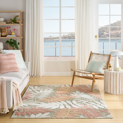 Bright coastal living room with sea view; pale sofa, pink cushions, tropical leaf rug, wicker chair, round side table.