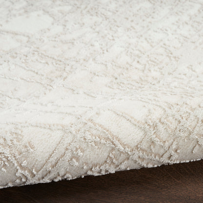 Cream-colored plush area rug with raised damask pattern, soft pile, edge visible on dark wood floor.