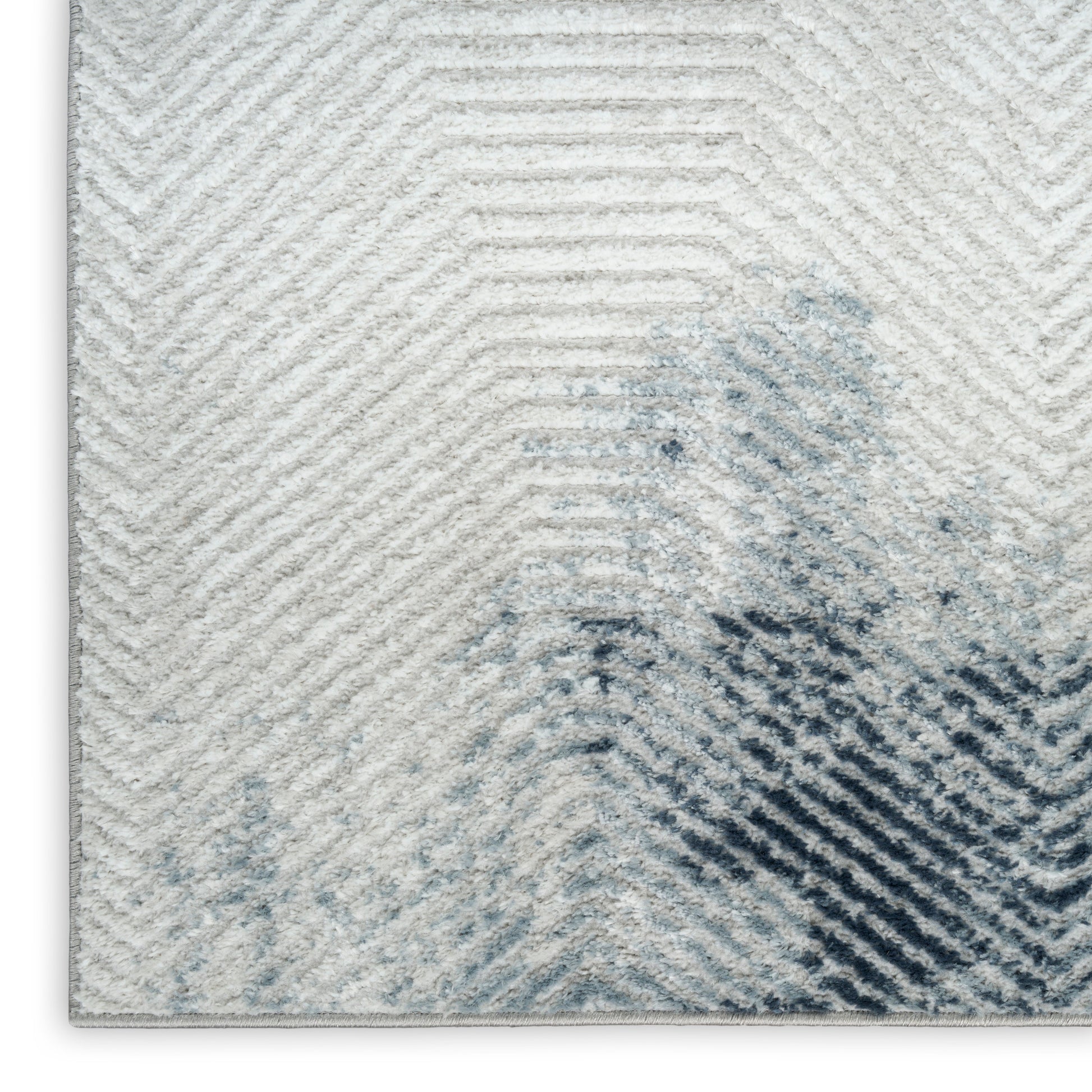 Rectangular light-gray rug with a raised chevron texture and blue watercolor blot motif, modern plush pile.