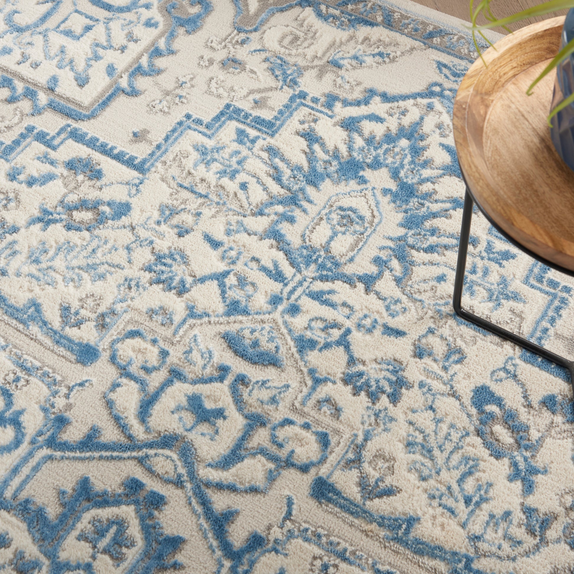 Blue and cream ornate patterned area rug with floral motifs; round wooden tray with a plant resting on the edge.