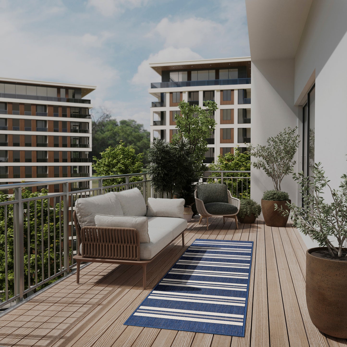 Modern balcony with wooden deck, beige cushioned sofa, gray armchairs, blue striped outdoor rug, and large potted plants.