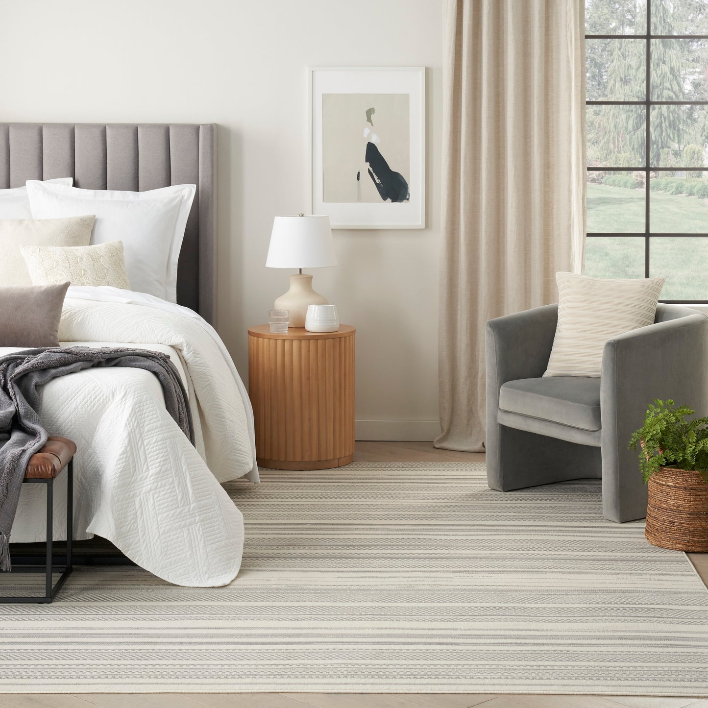 Neutral bedroom scene featuring a striped rug on the floor, with a gray upholstered bed and white quilt visible.