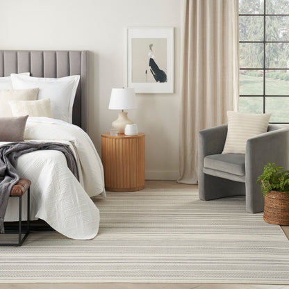 Neutral bedroom scene featuring a striped rug on the floor, with a gray upholstered bed and white quilt visible.