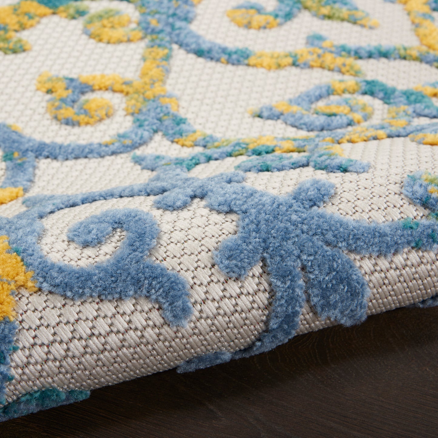 Close-up of beige rug with blue and yellow scroll floral pattern and plush textured pile.