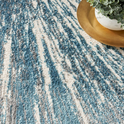 Blue and ivory abstract striped area rug with plush texture; gold tray and potted greenery at edge.