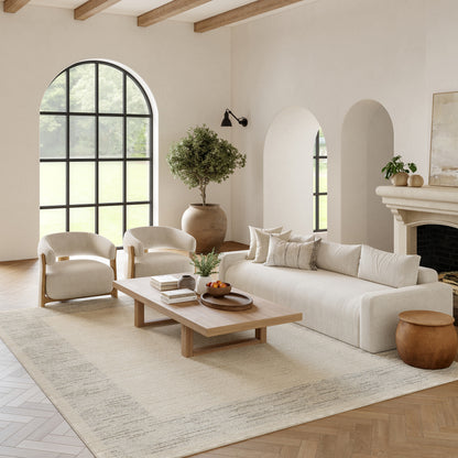 Bright living room with cream sofa, white curved chairs, wooden beams, an arched window, a potted plant, and a beige rug.
