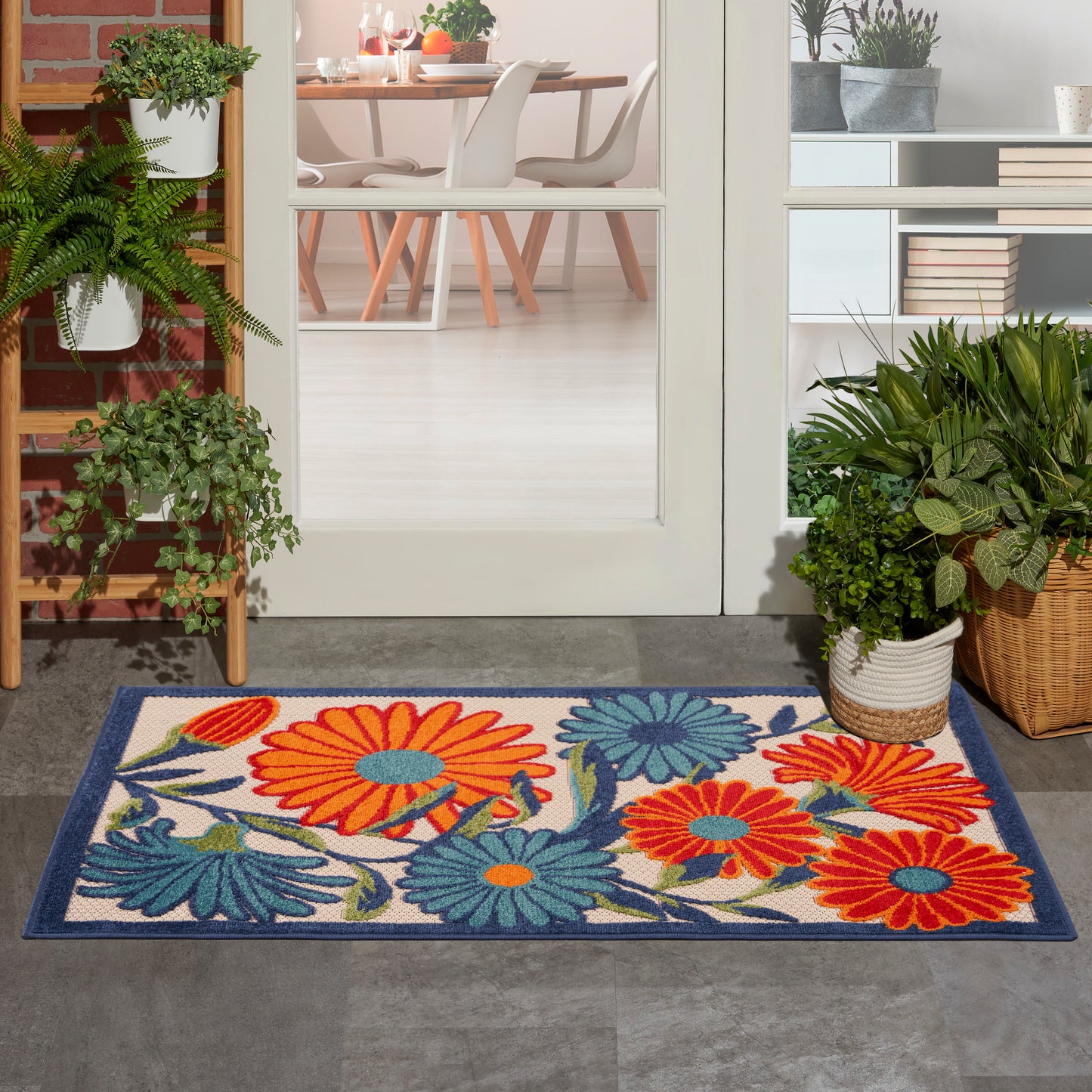 Rectangular outdoor rug with bright orange, teal and blue flowers on a cream background, dark blue border.