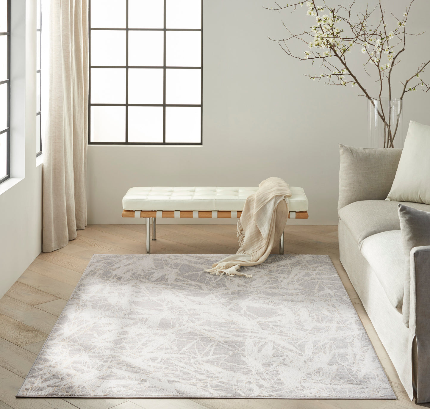 Neutral living room with pale patterned rug, ivory tufted bench, beige scarf, near large grid window & gray sofa.