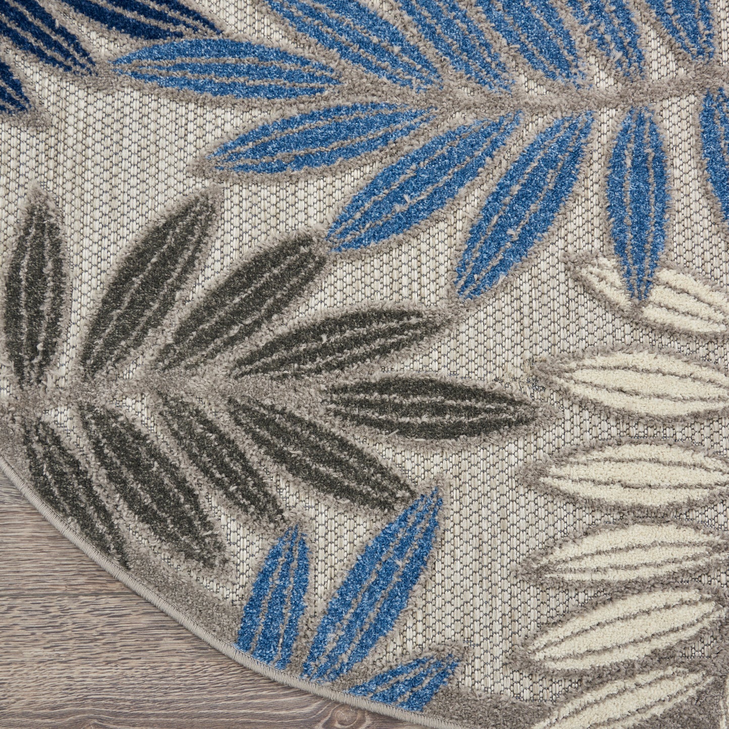 Round shag rug with blue, cream and gray leaf patterns on a beige textured background.