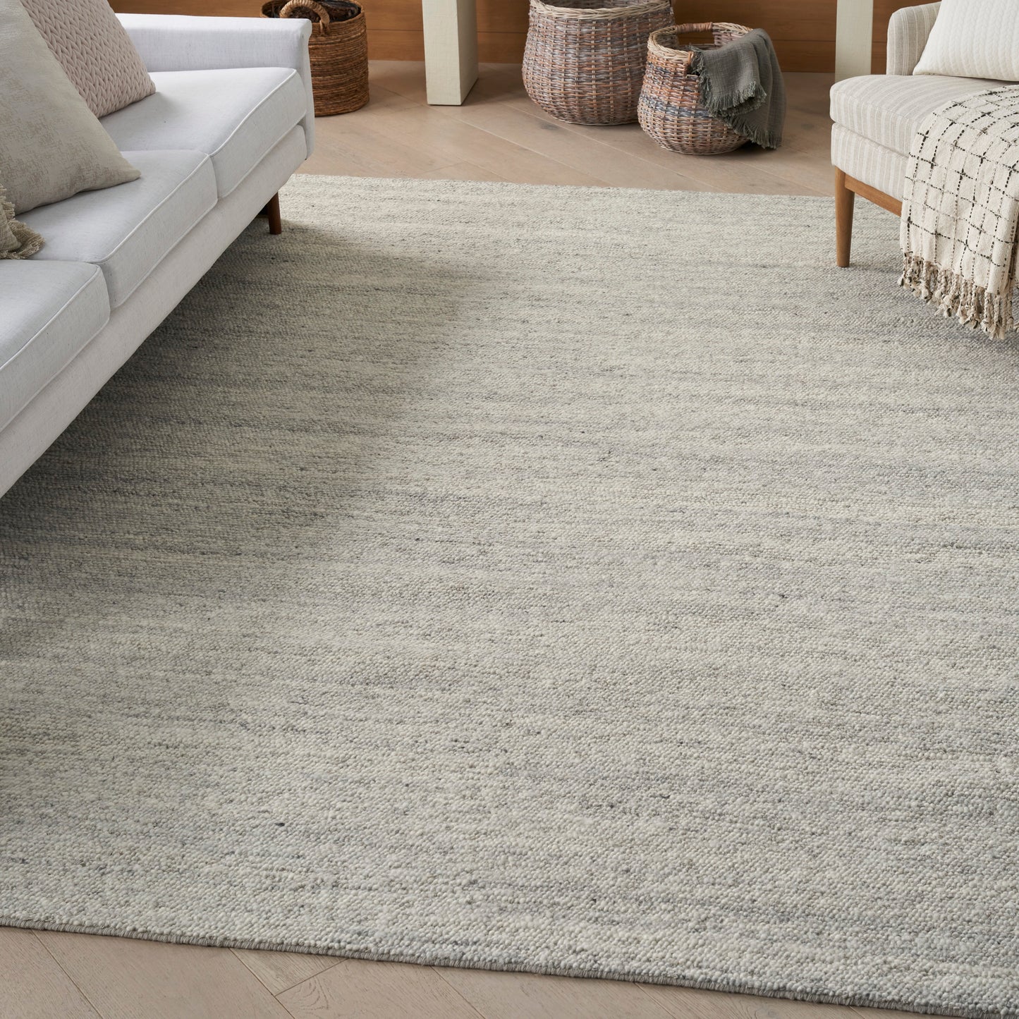 Neutral living room with light gray textured rug, pale sofa on left and woven baskets in back.