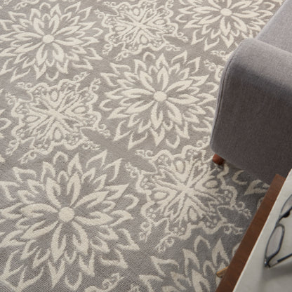 Gray area rug with large white floral/mandala motifs, paired with a gray sofa and wooden side table.