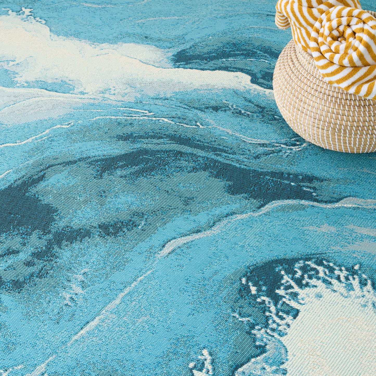 Turquoise ocean-wave patterned rug with a woven straw hat and a yellow striped cloth resting at the edge.