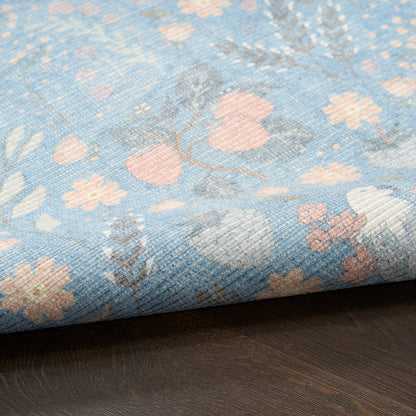 Blue floral woven rug with pale pink flowers and gray leaves, textured weave, folded edge on dark wood surface.