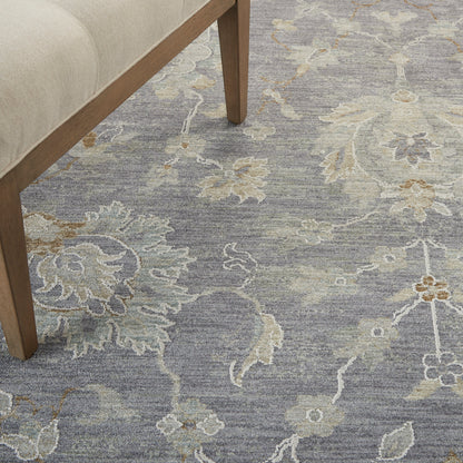 Blue-gray area rug with cream floral pattern under a wooden sofa leg.