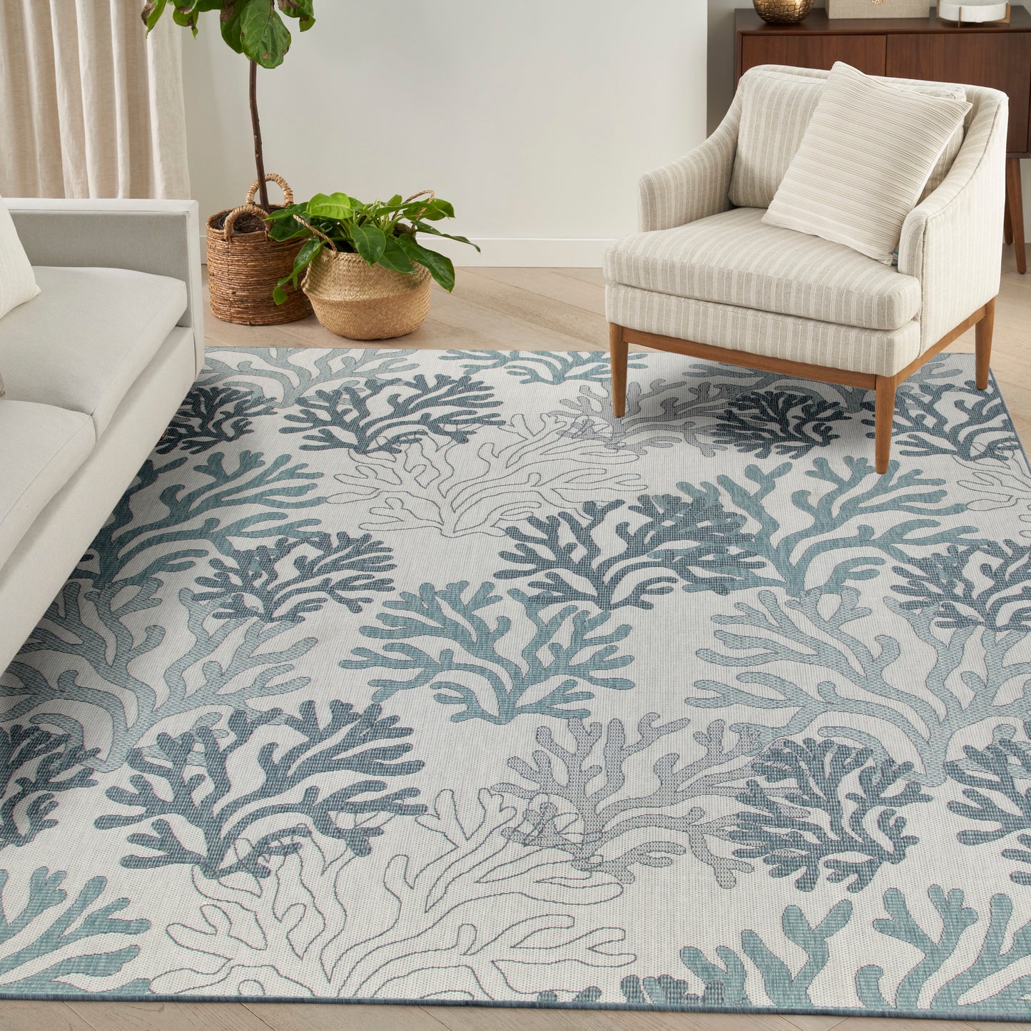 Light gray area rug with teal coral pattern, beige striped armchair, and potted plants in woven baskets.