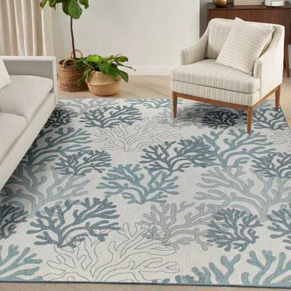 Light gray area rug with teal coral pattern, beige striped armchair, and potted plants in woven baskets.