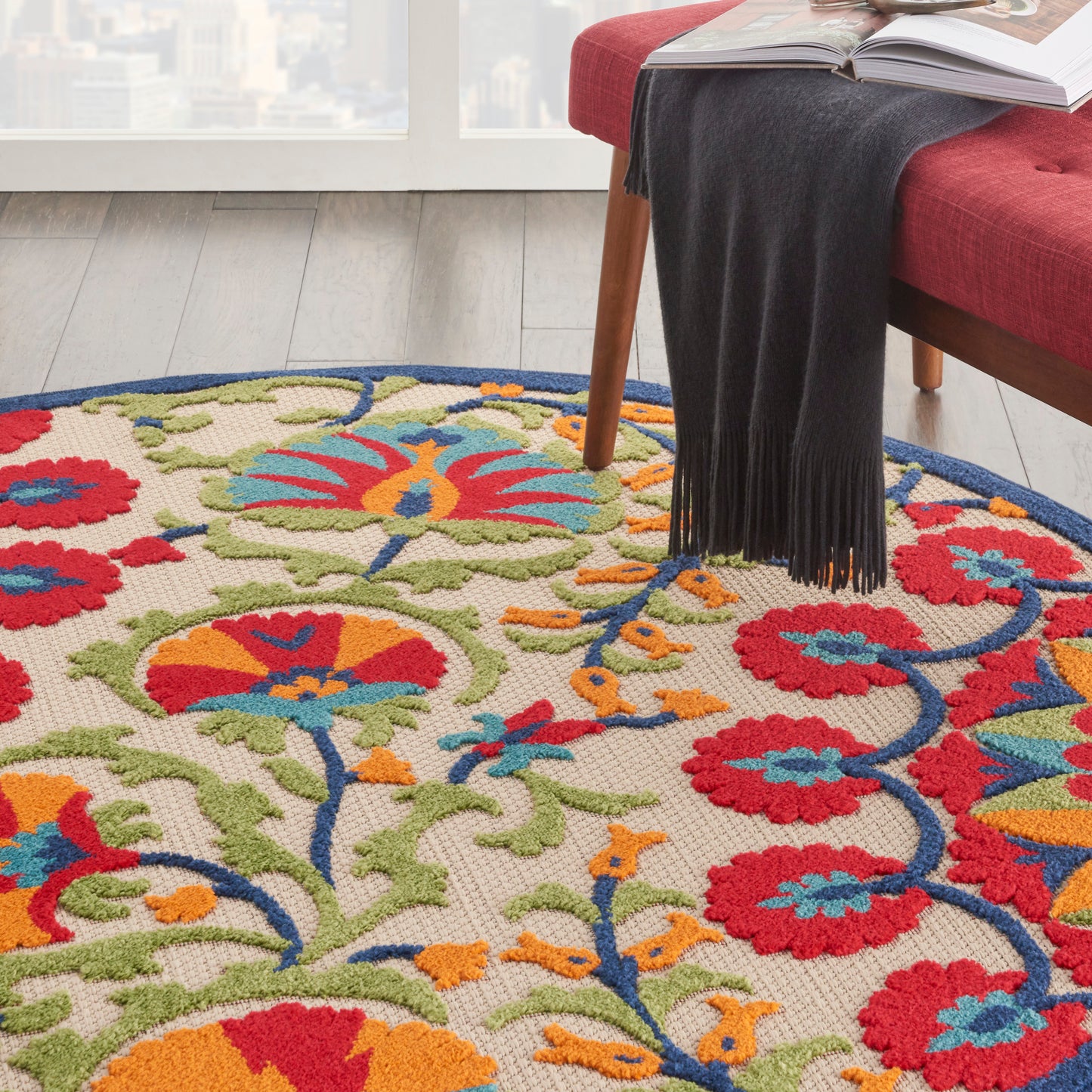 Round multicolor floral area rug on light wood floor beside a red sofa; red, blue, orange flowers with green vines.