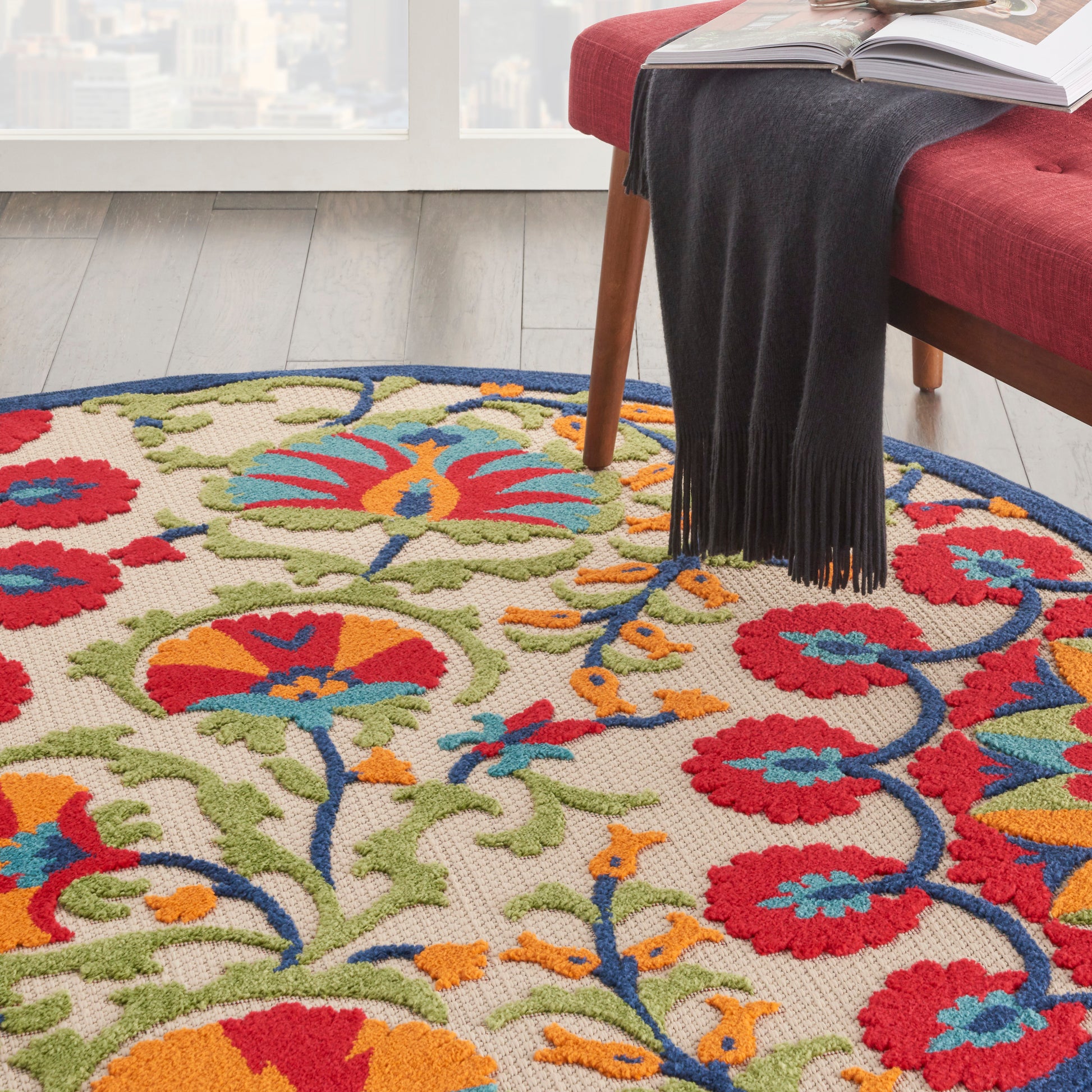 Round multicolor floral area rug on light wood floor beside a red sofa; red, blue, orange flowers with green vines.