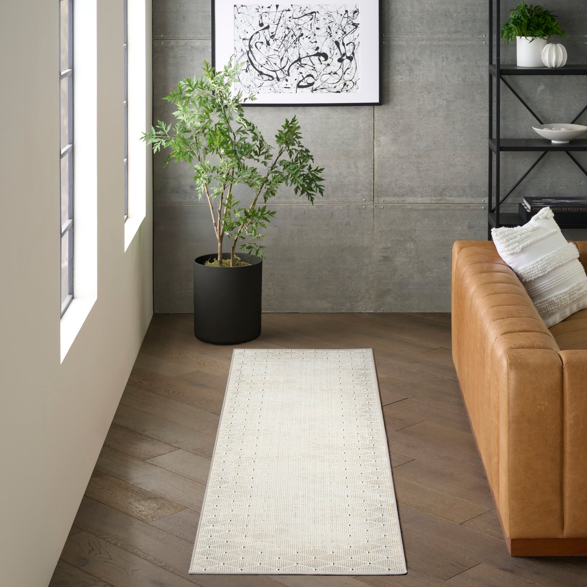 Long beige woven runner rug with a dotted border on a dark wood floor beside a tan leather sofa.