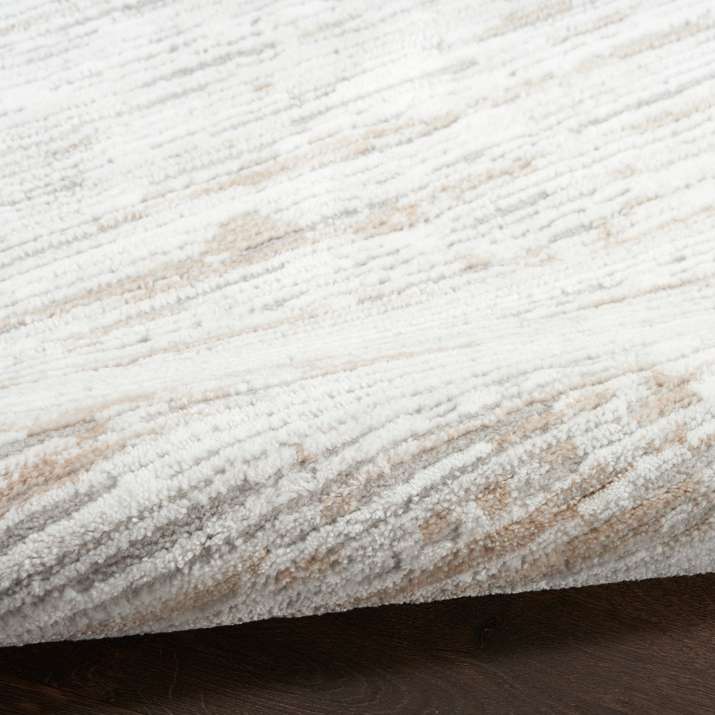 Cream-beige textured rug with plush pile and subtle gray stripes, rolled edge on dark wood floor.