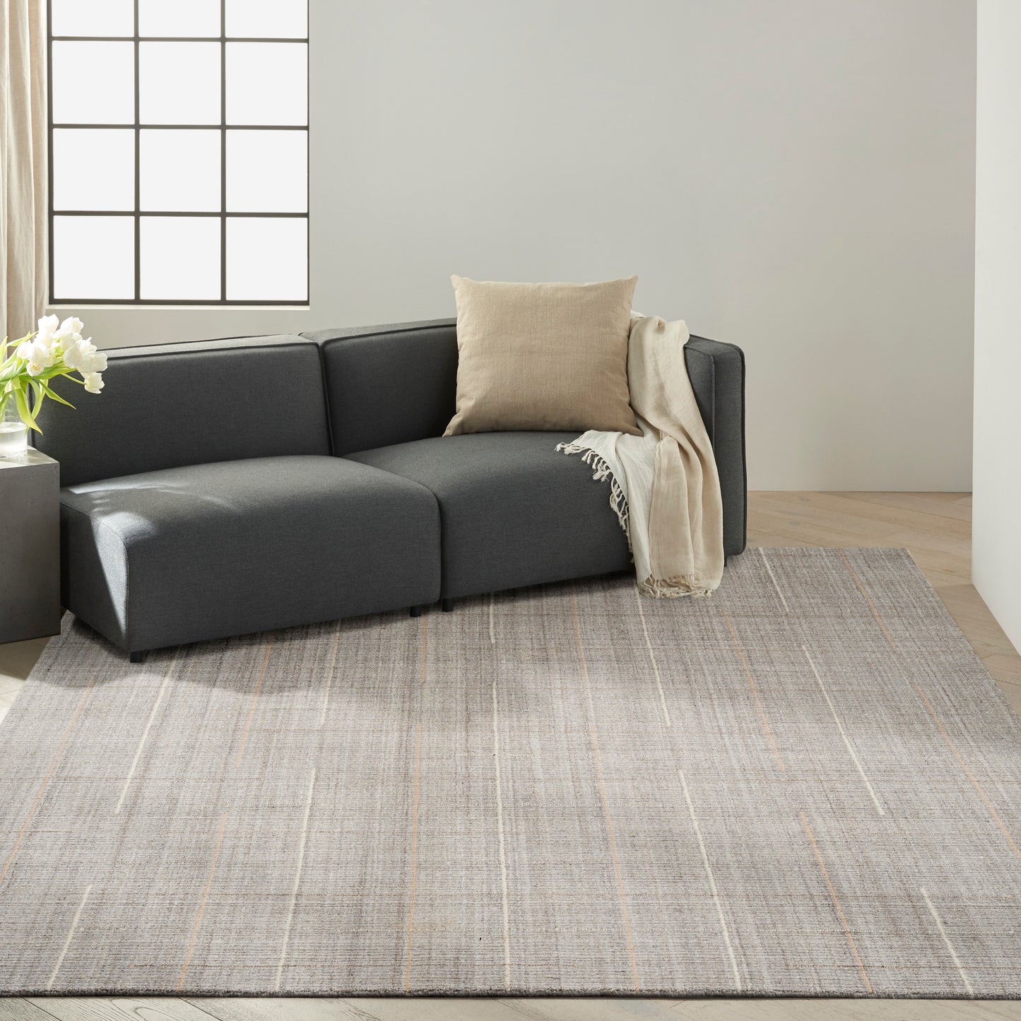 Dark charcoal modular sectional sofa with beige throw pillow and blanket on a light gray area rug in a modern living room.