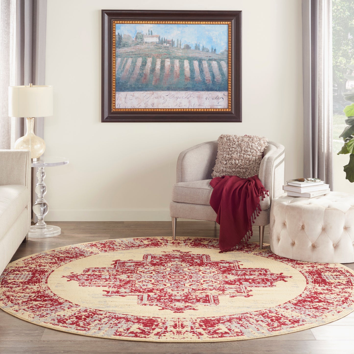 Round cream rug with red distressed medallion pattern; beige armchair with red throw, tufted ottoman, cozy living room.
