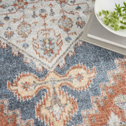 Colorful oriental area rug in ivory, blue and rust with medallion motifs; plant and books resting on edge. 4' x 6'.