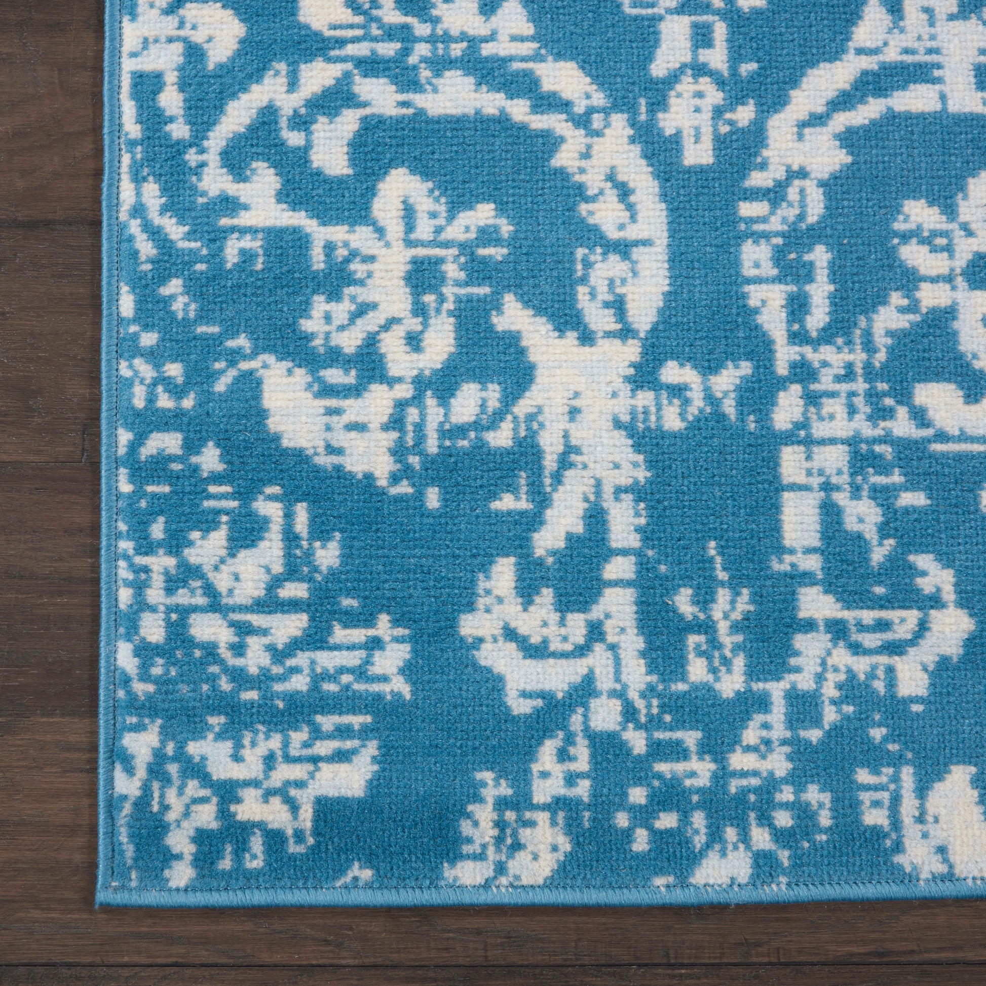 Turquoise blue rug with white distressed floral damask pattern and slim border on wood floor.