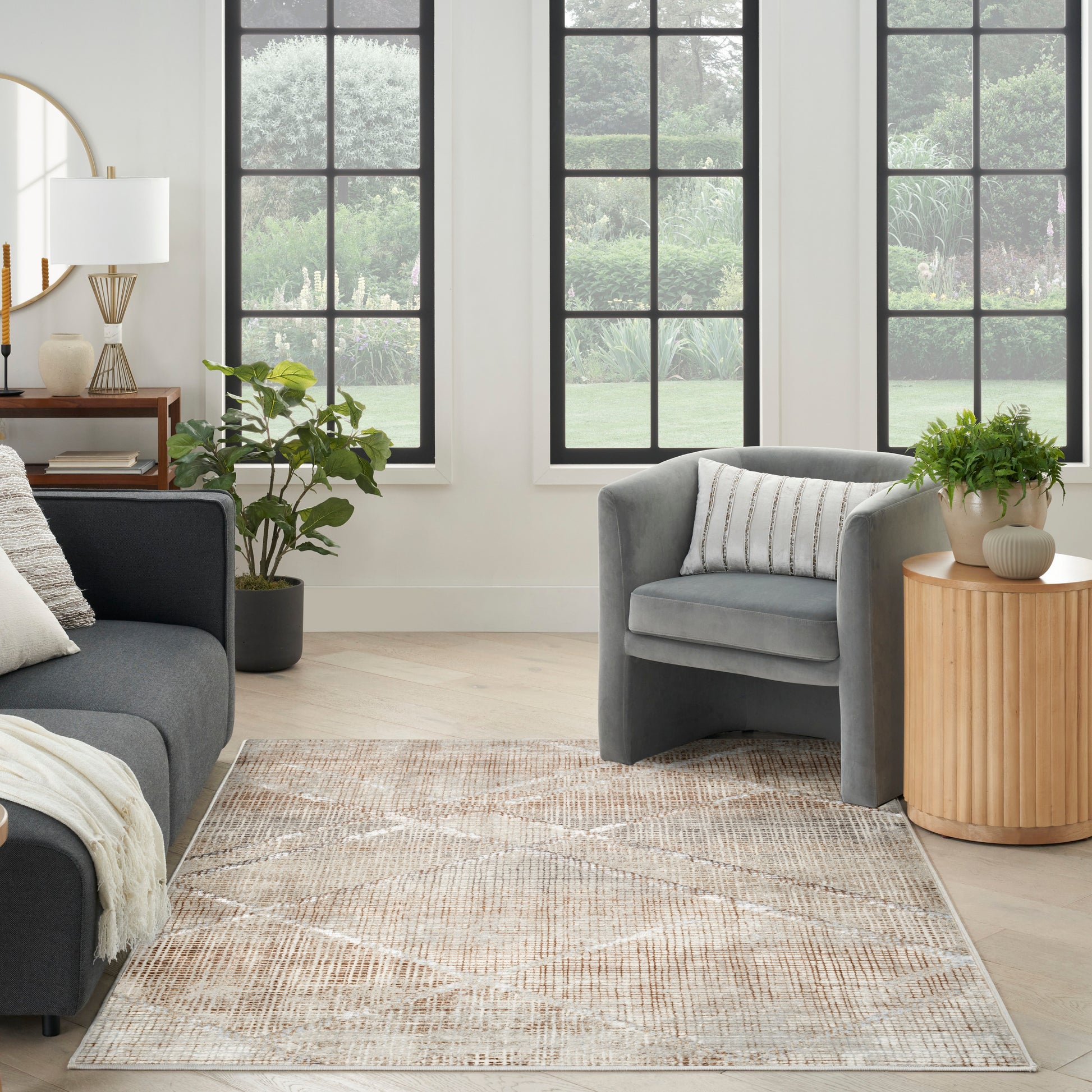 Cozy living room with gray upholstered sofa and armchair, beige patterned rug, wood side table, and plants near grid windows.