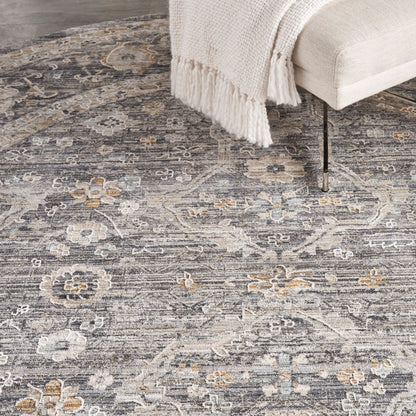 Muted floral grey area rug with ivory and pale blue accents under a beige sofa and cream fringed throw.