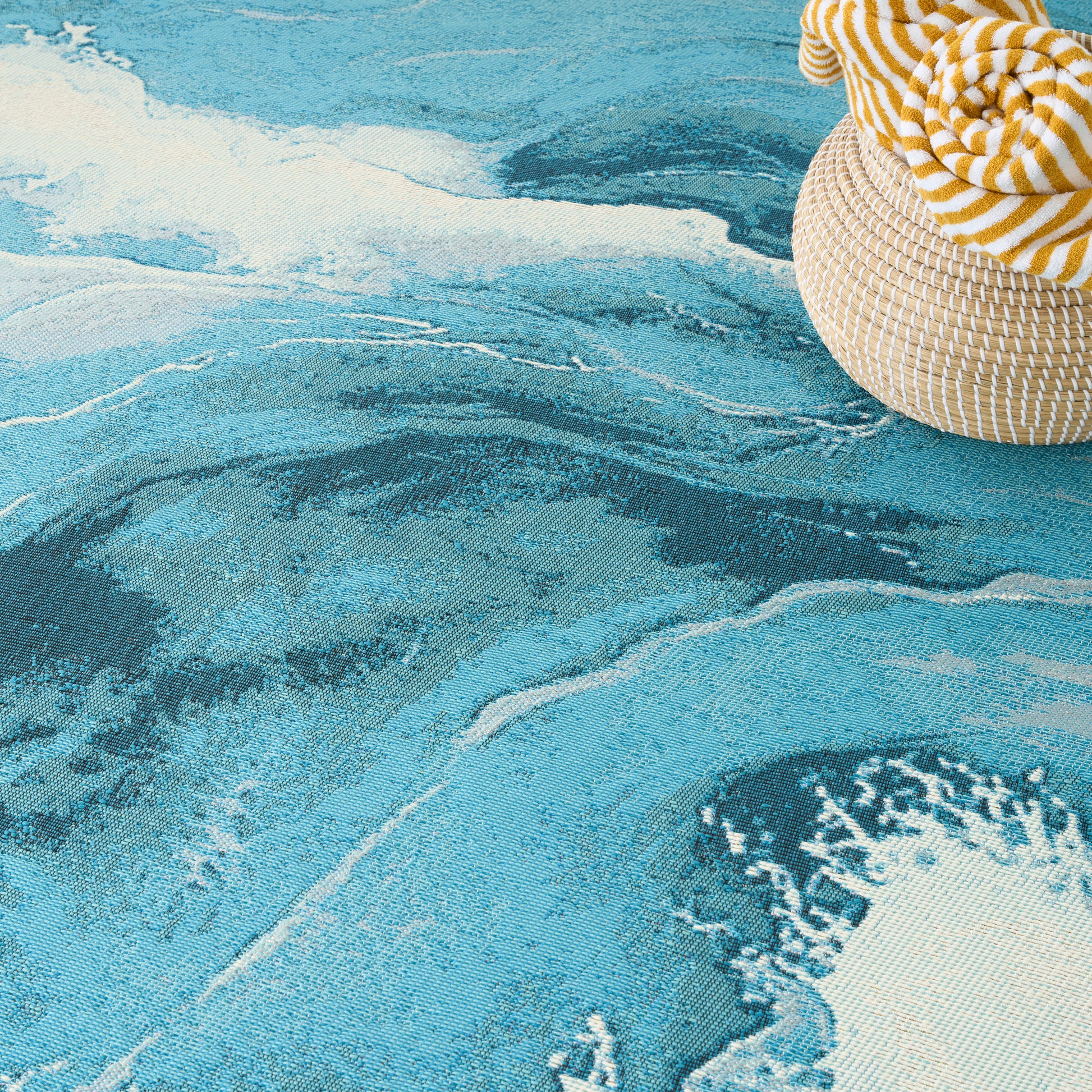 Turquoise wave-patterned rug with a woven straw hat and yellow striped fabric.